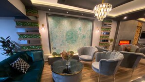 A modern living room with a green sofa, grey armchairs, a round coffee table, and a fireplace. - Grand Zara Otel (Kayseri)