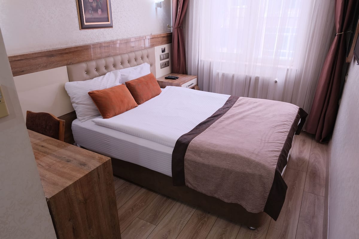 A hotel room with a large bed, wooden headboard, bedside tables, and a window with curtains.