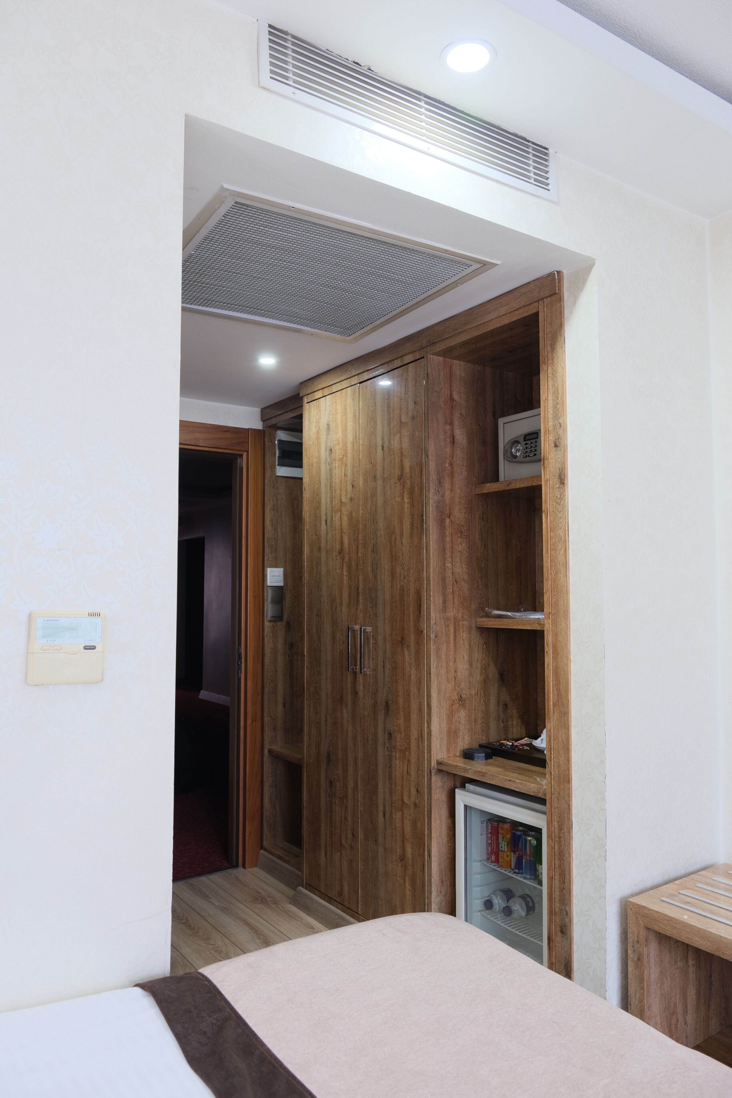 A bedroom with a bed, wooden wardrobe, built-in mini-fridge, and a small table.