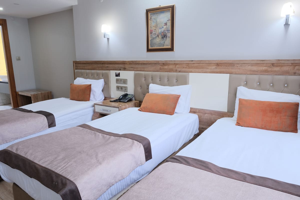 A hotel room with three beds, a wooden headboard, a painting on the wall, and a bedside table with a phone.