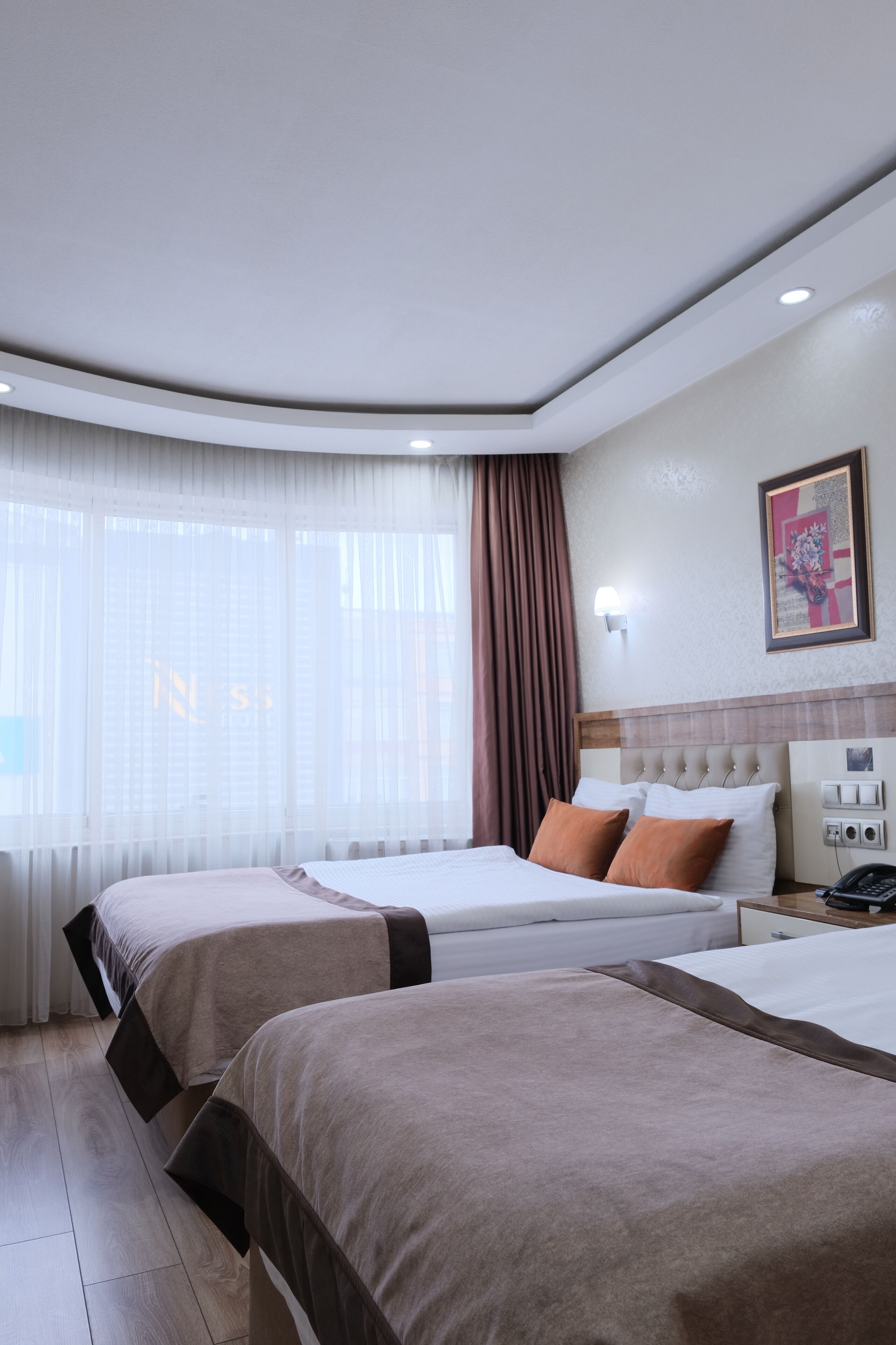 Une chambre d’hôtel avec deux lits, une table de chevet, une lampe fixée au mur et une fenêtre avec des rideaux.