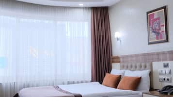 Ein Hotelzimmer mit zwei Betten, einem Nachttisch, einer Wandlampe und einem Fenster mit Vorhängen.