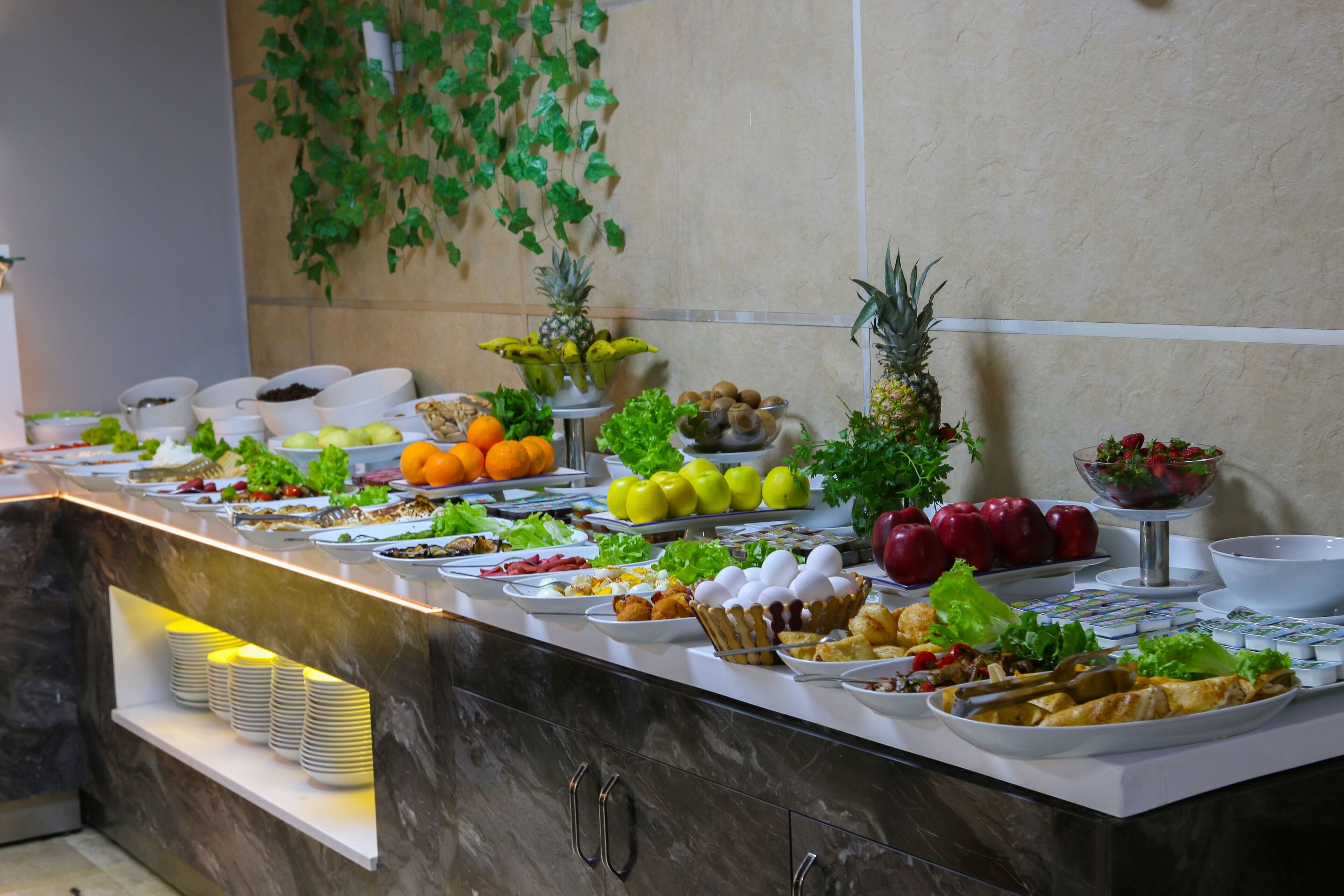 A buffet with various food items and a decorative wall with hanging plants.