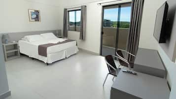 Quarto de hotel com cama, escrivaninha, poltrona, televisão e varanda com vista.