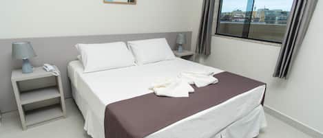 Una cama bien hecha con una colcha marrón, una lámpara de noche y un teléfono en la mesita de noche.