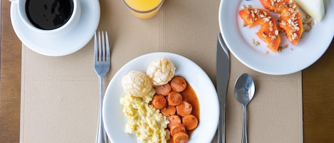 A breakfast setting with a plate of scrambled eggs, sausage slices, and a glass of orange juice.