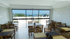 Ein Essbereich mit Tischen und Stühlen, Blick auf das Meer und Gebäude, sowie ein Balkon mit Glastüren.