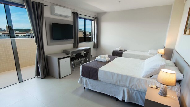 Ein Hotelzimmer mit Bett, Schreibtisch, Stuhl, Fernseher und einem Balkon mit Vorhängen.