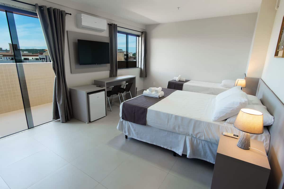 Ein Hotelzimmer mit Bett, Schreibtisch, Stuhl, Fernseher und einem Balkon mit Vorhängen.