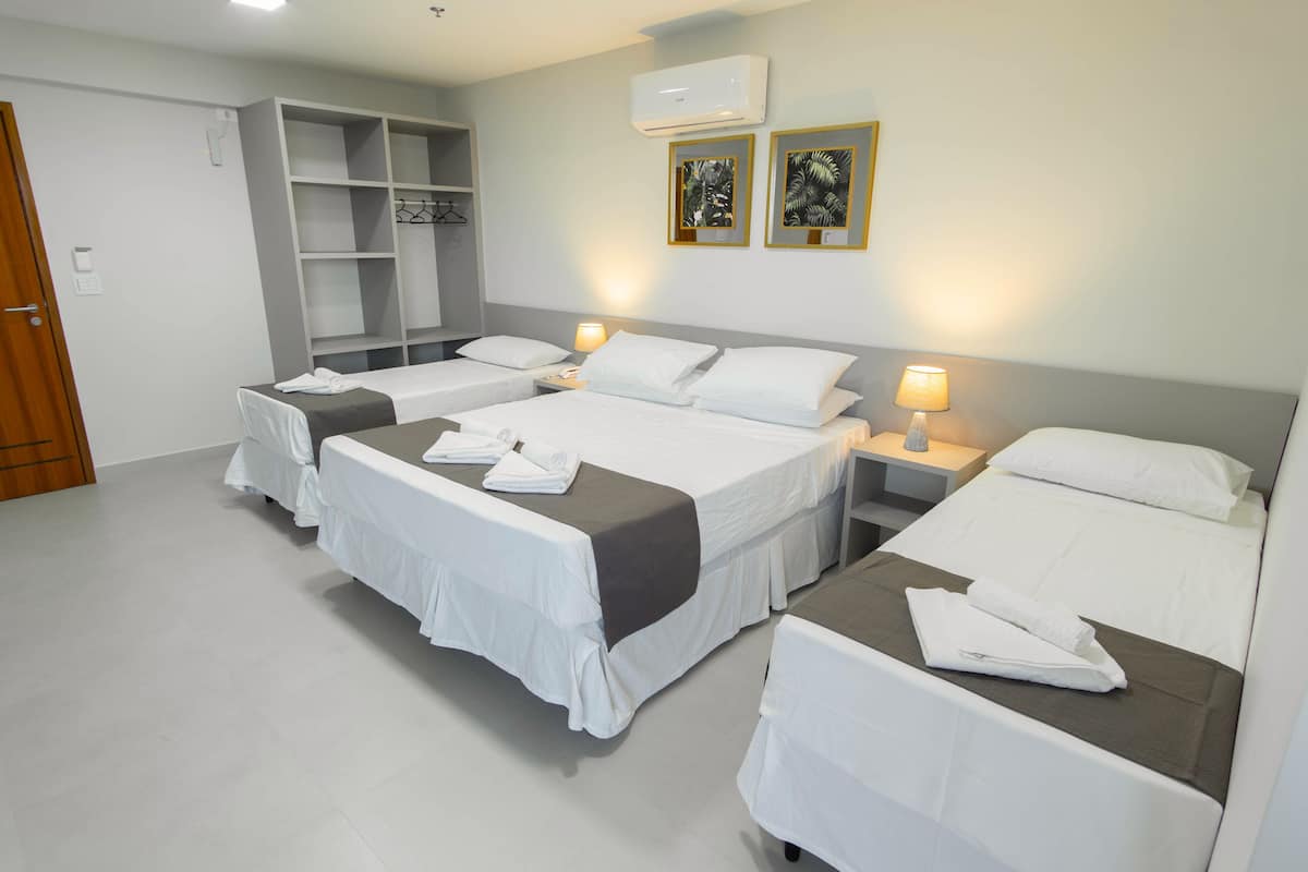 Ein Hotelzimmer mit vier nebeneinander stehenden Betten, einem Kleiderschrank und zwei wandmontierten Klimaanlagen.
