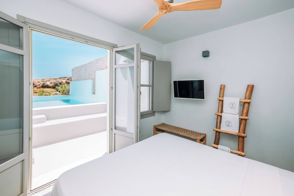 A bedroom with a bed, a TV, a wooden ladder, and a view of a pool and landscape.