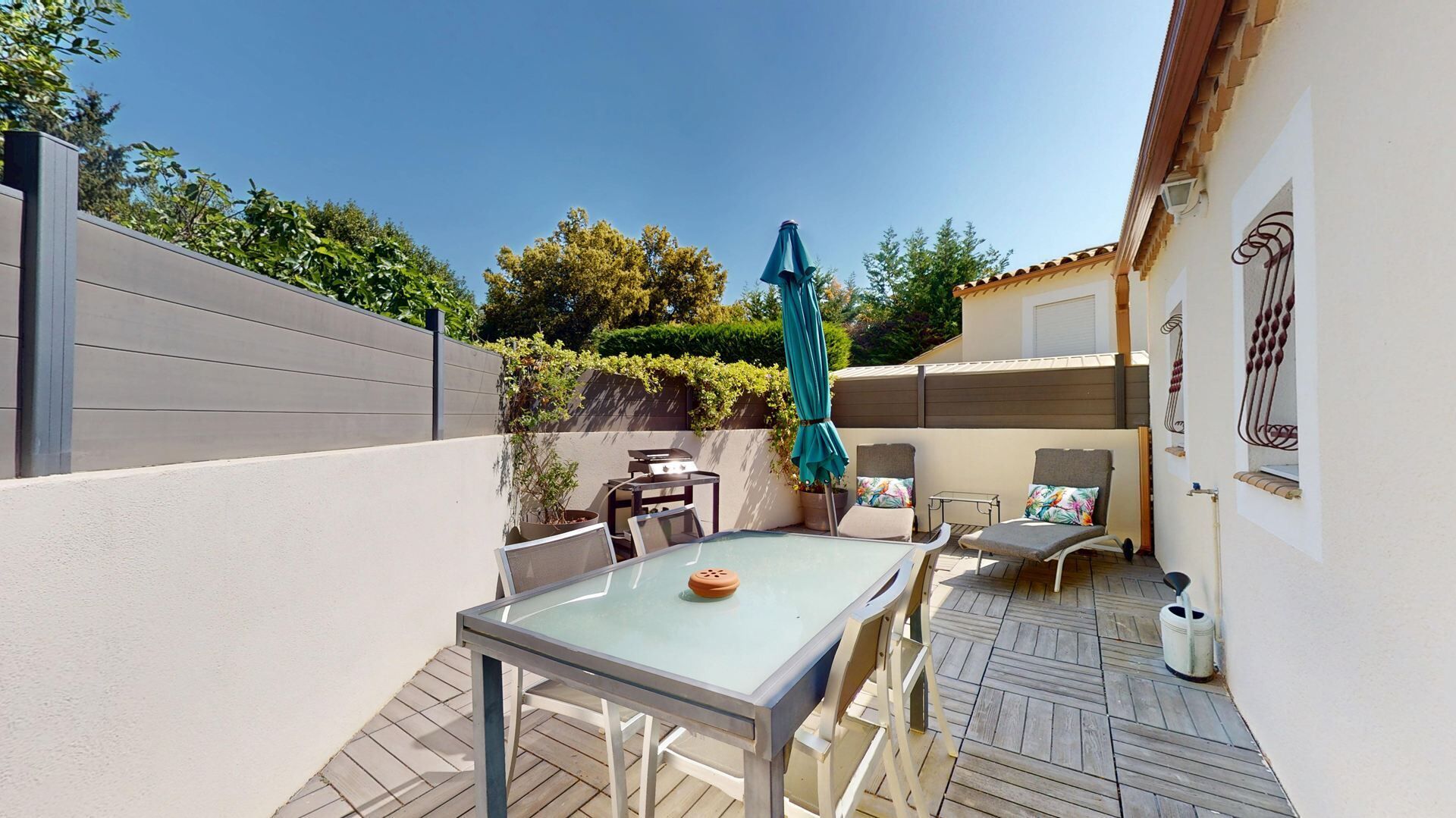 Une terrasse avec une table et des chaises, un barbecue et un parasol bleu.