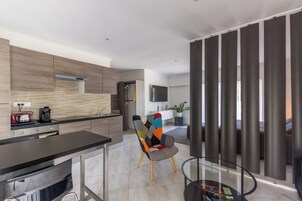 Uma cozinha moderna com bancada preta, uma cadeira colorida e uma mesa de vidro.