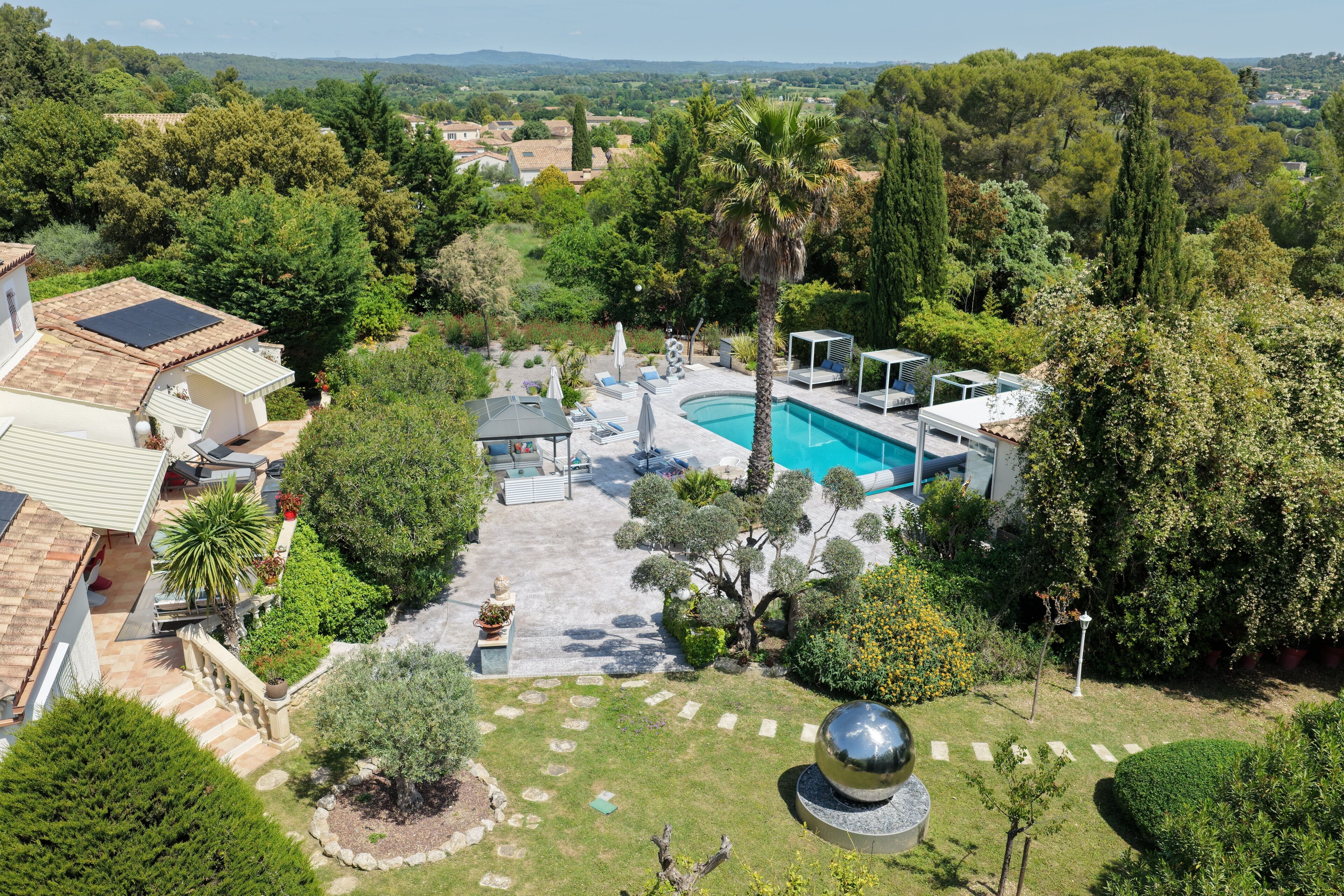 A residential property with a swimming pool, garden, and a view of the surrounding landscape.