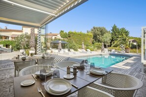 Un comedor con vista a la piscina, mobiliario exterior y una pérgola.