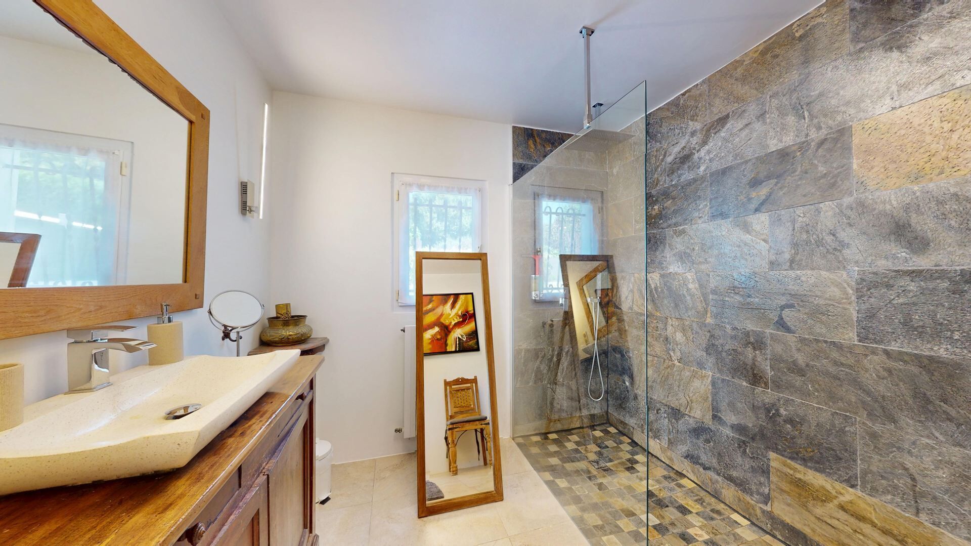 Un baño moderno con un espejo grande, un lavabo y una zona de ducha con paredes de piedra.