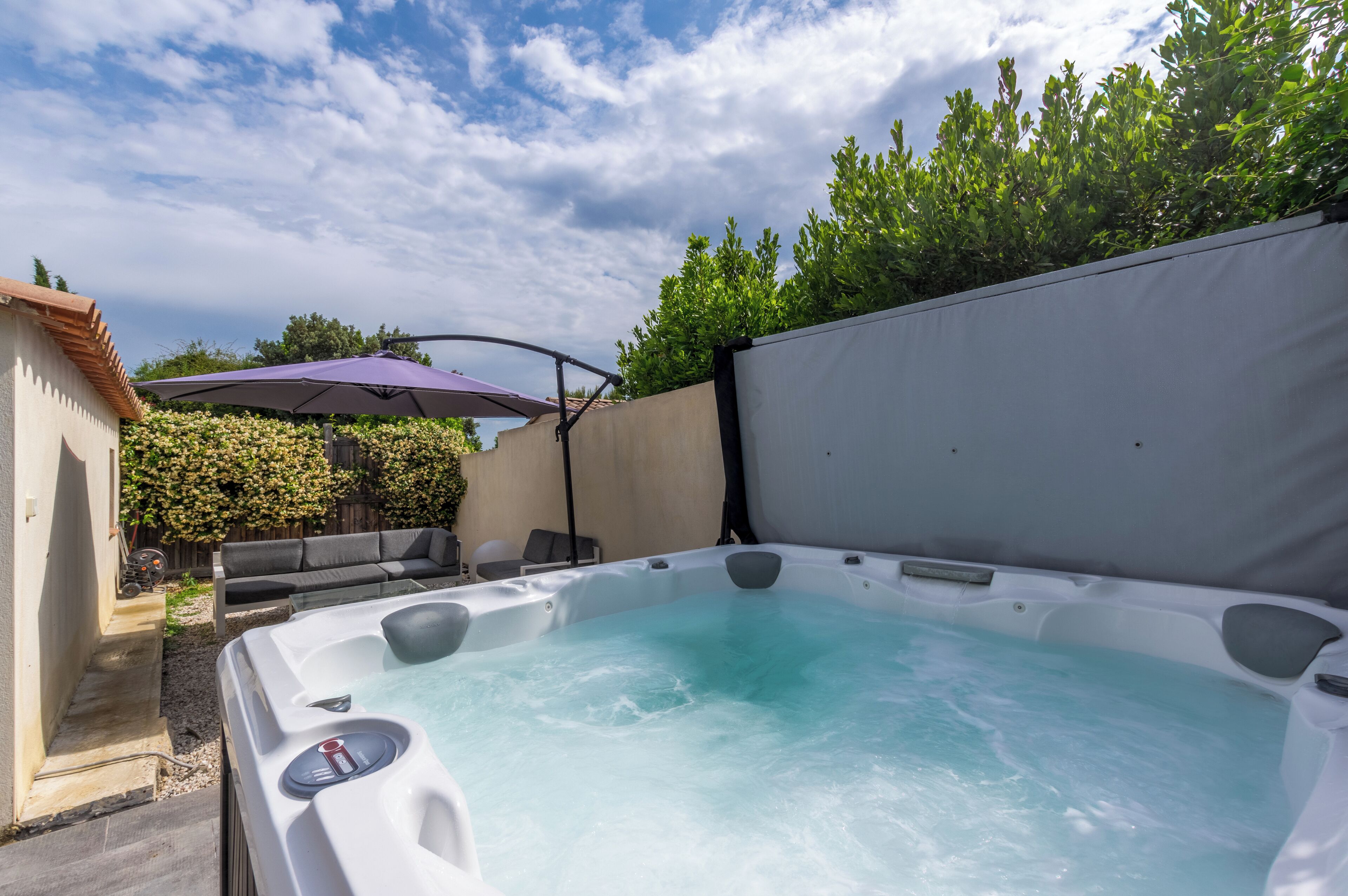 A hot tub with a patio area, including a sofa and an umbrella.