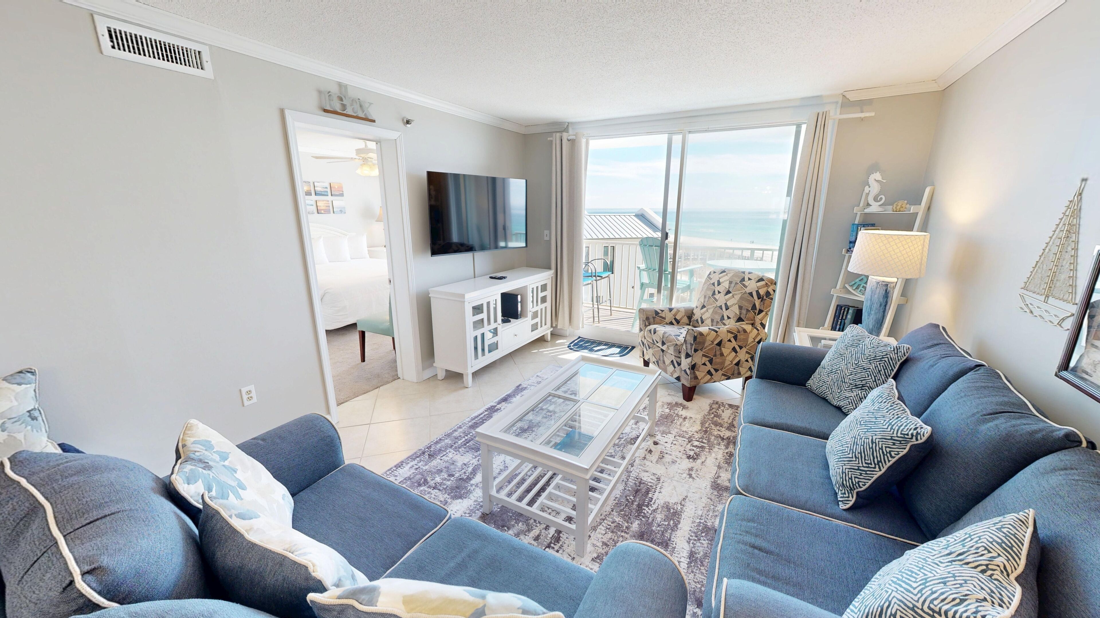 Un salon moderne avec un canapé, un téléviseur et une vue sur la mer grâce à de grandes fenêtres.