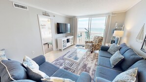 Una sala de estar moderna con un sofá, televisión y vistas al mar a través de amplios ventanales.
