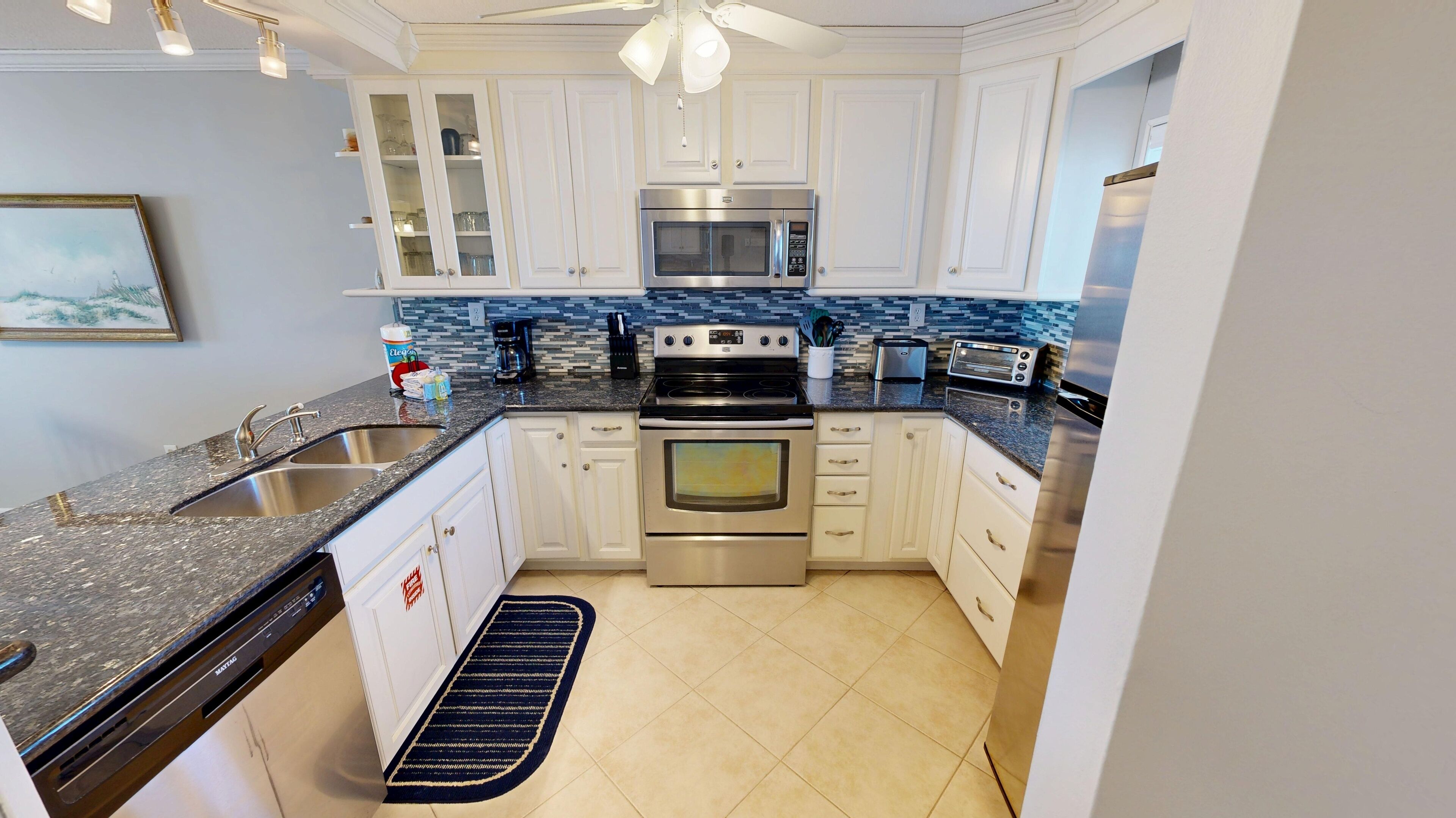 A modern kitchen with white cabinets, stainless steel appliances, and a blue backsplash.