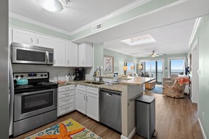 A modern kitchen with stainless steel appliances, white cabinetry, and a colorful rug. - Recently Renovated, oceanfront condo + Free Attraction Tickets! (Myrtle Beach)