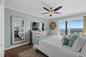A bedroom with a bed, a dresser, a television, a ceiling fan, a large mirror, and a view of the ocean. - Recently Renovated, oceanfront condo + Free Attraction Tickets! (Myrtle Beach)