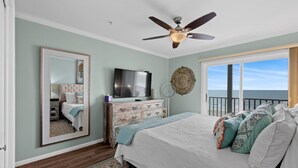 Une chambre à coucher comprenant un lit, une commode, un téléviseur, un ventilateur de plafond, un grand miroir et une vue sur l’océan.