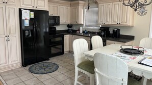 Une cuisine avec des meubles de couleur claire, un réfrigérateur noir, une cuisinière et une table à manger avec des chaises.