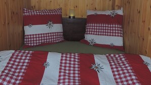 A wooden-paneled room with a bed featuring red and white checkered bedding and floral pillows. - Lovingly furnished Alphüttli (Wilderswil)