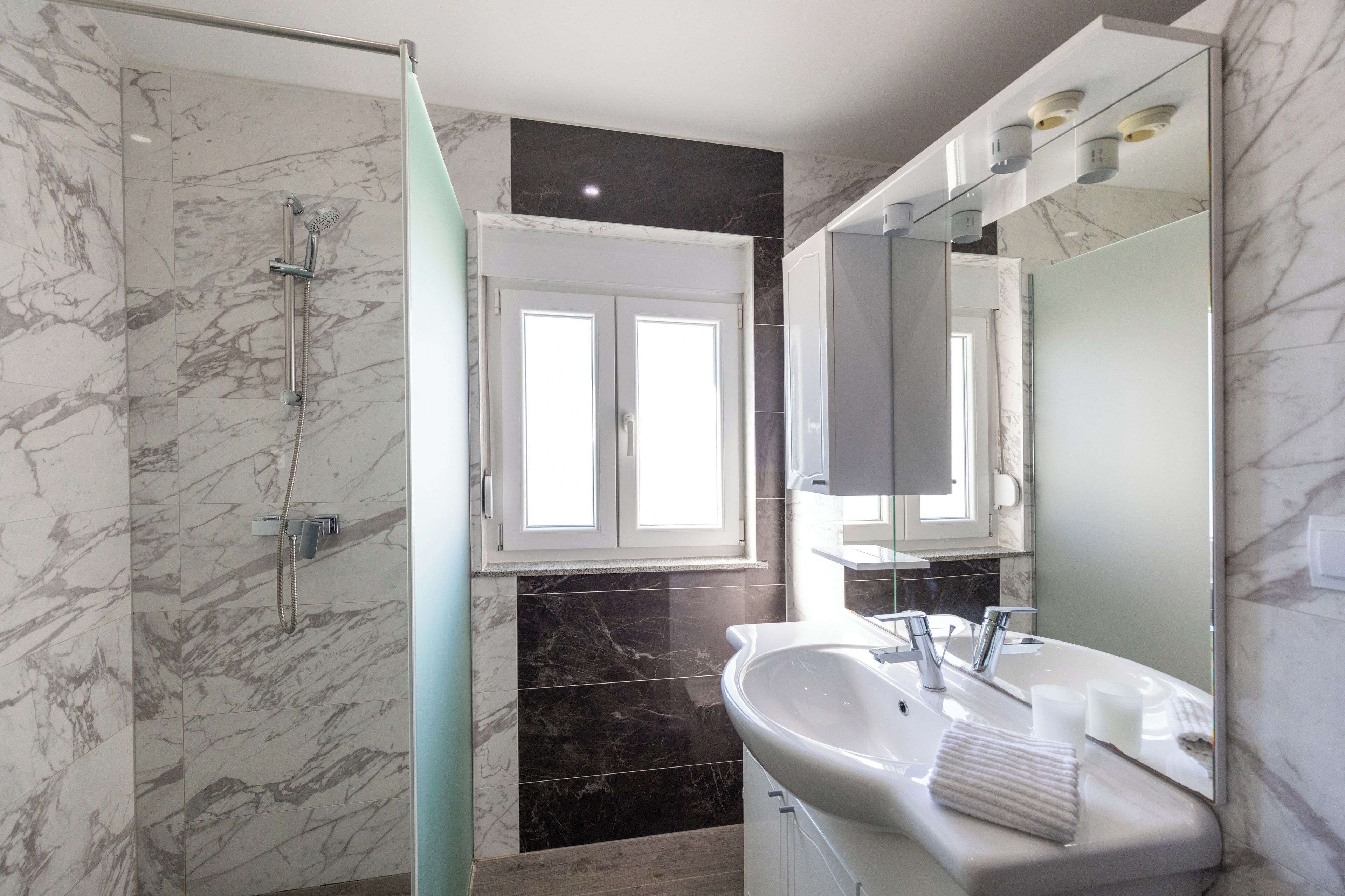 Un baño moderno con ducha envuelta en vidrio, un espejo grande y un lavabo blanco.