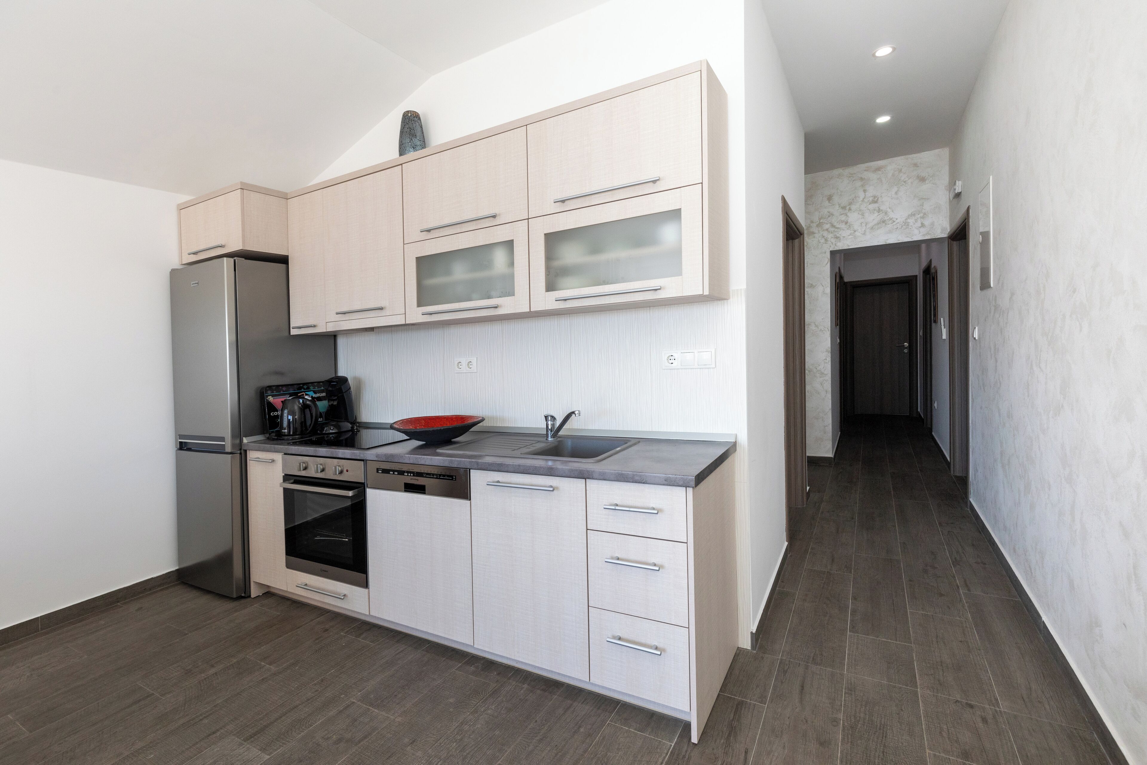 A modern kitchen with light wood cabinetry, stainless steel appliances, and a dark countertop.