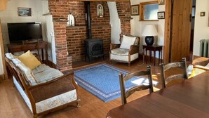 Un salon chaleureux avec une cheminée en briques, un téléviseur et des fauteuils confortables.