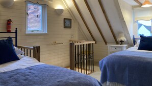 Une chambre confortable située sous les toits, avec deux lits, des poutres en bois, une fenêtre offrant une belle vue, un extincteur et une petite table de chevet avec une lampe.