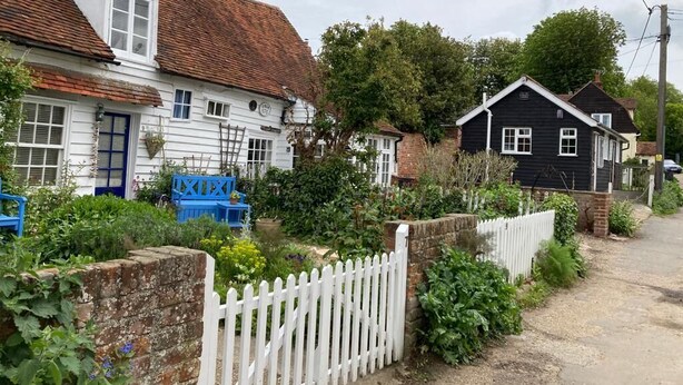 Une rue résidentielle bordée de maisons, avec une clôture blanche en bois et une chaise bleue dans le jardin.