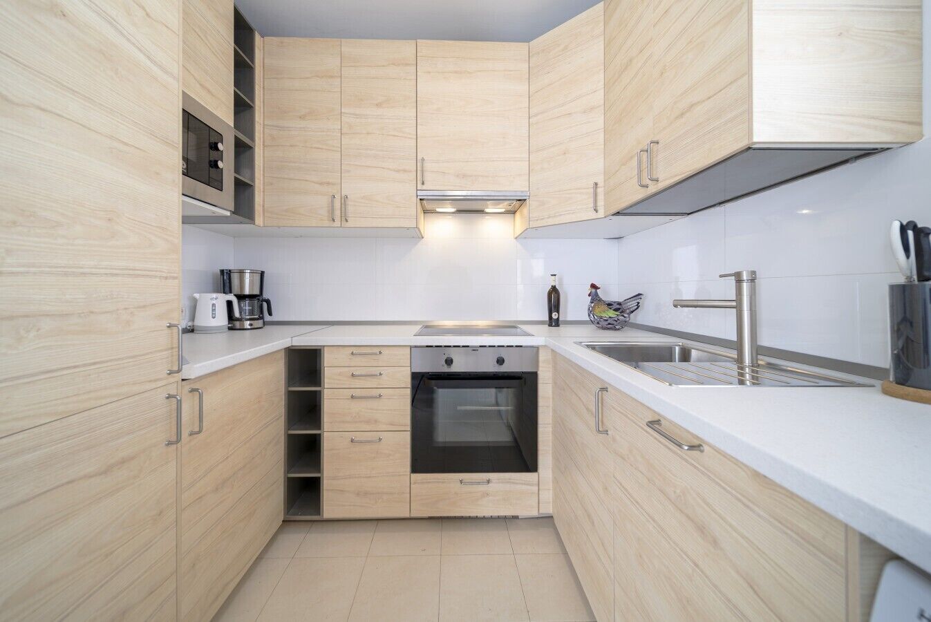 Cocina compacta con armarios de madera, horno empotrado, cafetera y pileta de acero inoxidable.