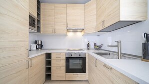 Eine kleine Küche mit Holzausstattung, einem Einbauofen, einer Kaffeemaschine und einem Edelstahl-Spülbecken.
