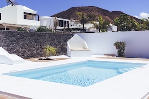 A swimming pool with a white deck, a stone wall, and a chair.
