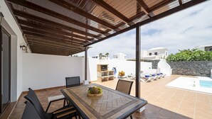 Eine Terrasse im Freien mit Tisch, Stühlen, einem Grill und einem Poolbereich.