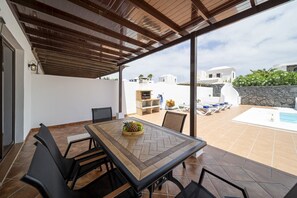 An outdoor patio with a table, chairs, a grill, and a pool area. - Villa Turquesa (Playa Blanca)