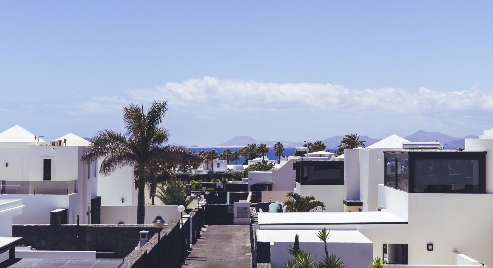 A residential area with modern white buildings, a clear sky, and distant mountains.
