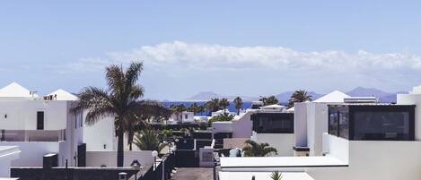 A residential area with modern white buildings, a clear sky, and distant mountains.