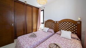 Ein Schlafzimmer mit zwei Betten, einem Kleiderschrank, einer Deckenleuchte und einem Fenster mit Vorhängen.