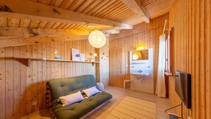 Une pièce chaleureuse, aménagée dans un chalet en bois, avec un canapé, un téléviseur et un plafond en bois.