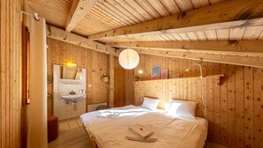 Une pièce aux murs lambrissés, comprenant un lit, un lavabo et un miroir.
