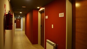 A corridor with red walls, numbered doors, and a fire extinguisher on the left. - Hotel Bait (General Roca)
