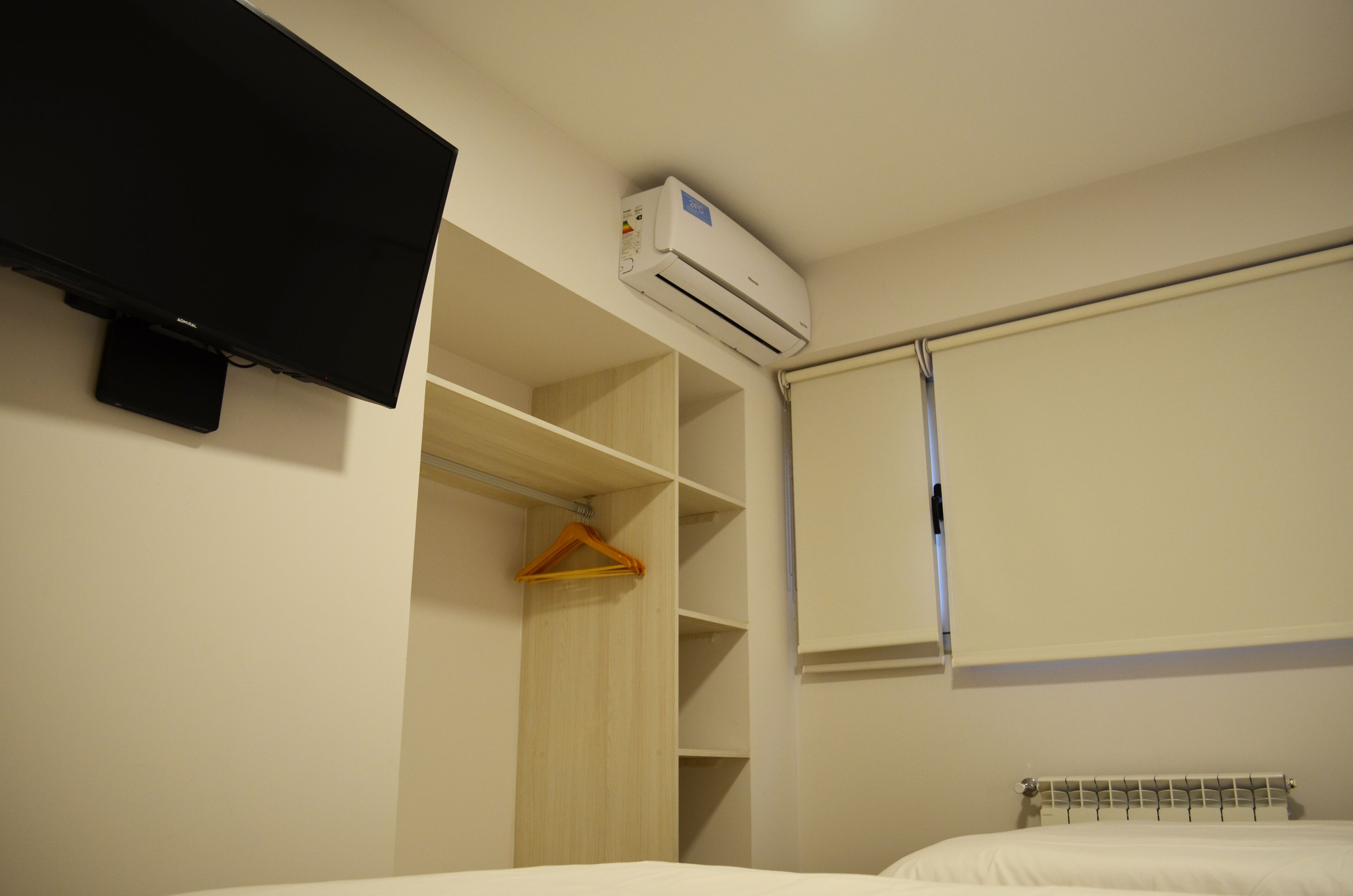 Quarto de hotel com cama, televisão na parede, guarda-roupa e janela com cortina.