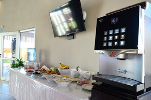 A buffet setup with a coffee machine, a TV, and various food items.