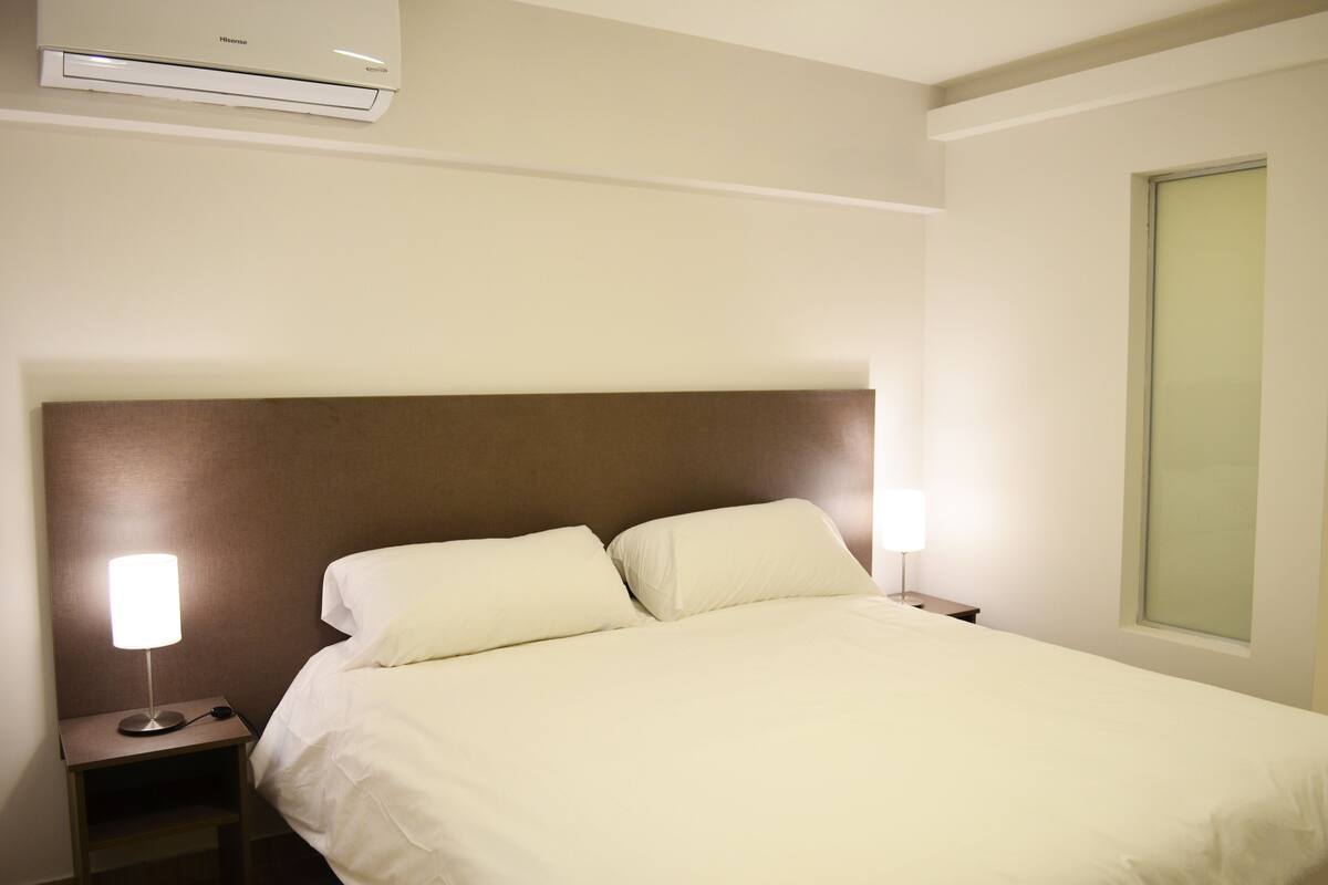 Une chambre d’hôtel avec un lit, deux lampes de chevet, une table de chevet et une fenêtre.