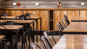A restaurant with wooden tables and black chairs, a counter with a decorative star and flowers, and a view of the kitchen through a glass partition. - Hotel Bait (General Roca)
