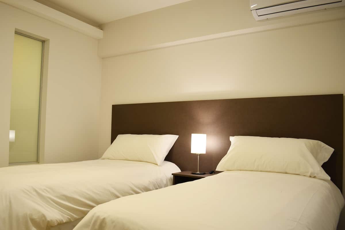 Une chambre d’hôtel avec deux lits, une table de chevet avec une lampe et un appareil de climatisation fixé au mur.